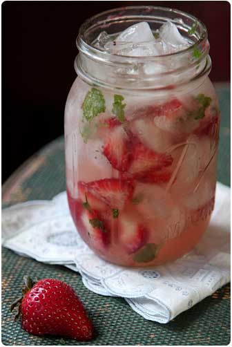 An image of a summer cocktail made with strawberries and moonshine served in a mason jar.