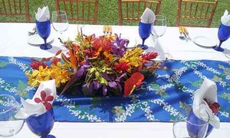 Maui catering table setting with blue glasses, wedding flowers and cloth table runner.