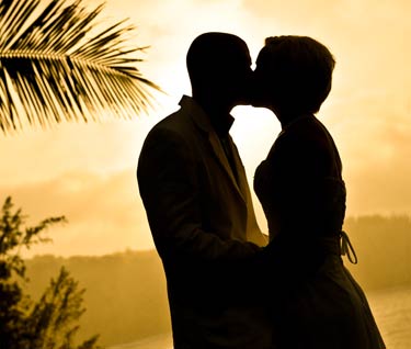 A newlywed couple first kiss at a sunset beach wedding on Maui.