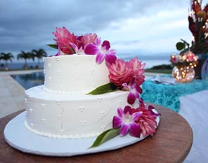 A double tiered Maui wedding cake with ivory fondant frosting and fresh flower orchids and ginger.