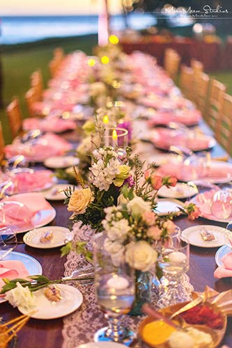 A Kings table setting with everyone at a single table for a Maui wedding reception with pink napkins and flowers.